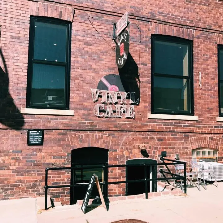 The Vinyl Grind storefront at 303 Kellogg Ave, with the record-shaped Vinyl Cafe sign on the brick wall